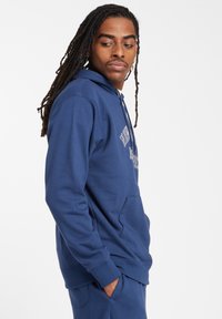 Felpa con cappuccio blu navy con tasca a marsupio, polsini a costine e cappuccio regolabile. Presenta il logo testuale sul petto. Tessuto morbido e texturizzato.