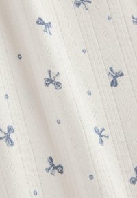 Bomuldsstof med hvid baggrund, prydet med lyseblå sløjfer, prikker og teksturerede striber, hvilket skaber et diskret mønster.