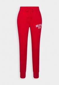 Röda träningsbyxor med elastisk midja, justerbar dragsko och vit "HOLLISTER"-logotyp på vänster lår. Mjukt material, smala ben.