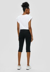 Haut blanc à manches courtes et pantalon noir court, avec une coupe ajustée, des ourlets roulés et une texture lisse. Associé à des baskets blanches.