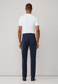 Marineblauwe broek met een smal model, voorzien van zijzakken en achterzakken. G gedragen met een witte kortemouwen shirt en bruine schoenen.