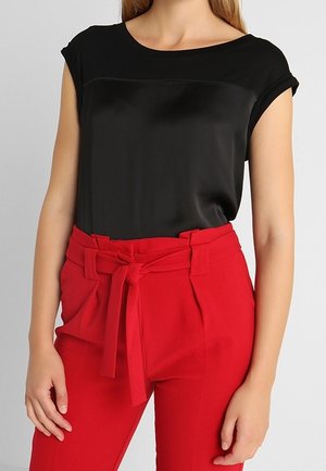 Schwarzes Satin-T-Shirt mit aufgekrempelten Ärmeln, kombiniert mit hoch taillierten roten Hosen mit gebundenem Stoffgürtel und strukturierten Falten.