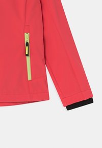 Manga de casaco vermelho com bolso com fecho verde e punho interior preto visíveis sobre fundo branco.