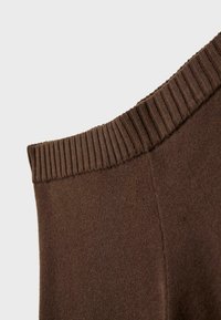 Gros plan sur un tissu en maille marron avec une ceinture élastique côtelée, mettant en valeur la texture et les détails de la couture.