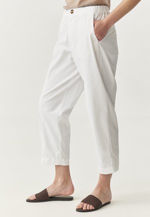 Witte katoenen broek met een elastische tailleband, voorzakken en een knoopdetail. Gecombineerd met bruine platte sandalen.