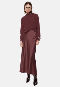 Maglione bordeaux con collo alto e maniche lunghe, abbinato a una gonna di raso coordinata. Le calzature consistono in stivali neri lucidi con punta a stiletto.