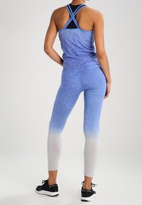 Top in interlock blu scuro con spalline incrociate, abbinato a leggings ombre blu-bianco. Indossato con scarpe da corsa nere.