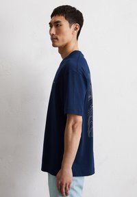Marineblauwe katoenen t-shirt met korte mouwen, met een lijnpatroon aan de achterkant. Ronde hals, losse pasvorm en zachte textuur.