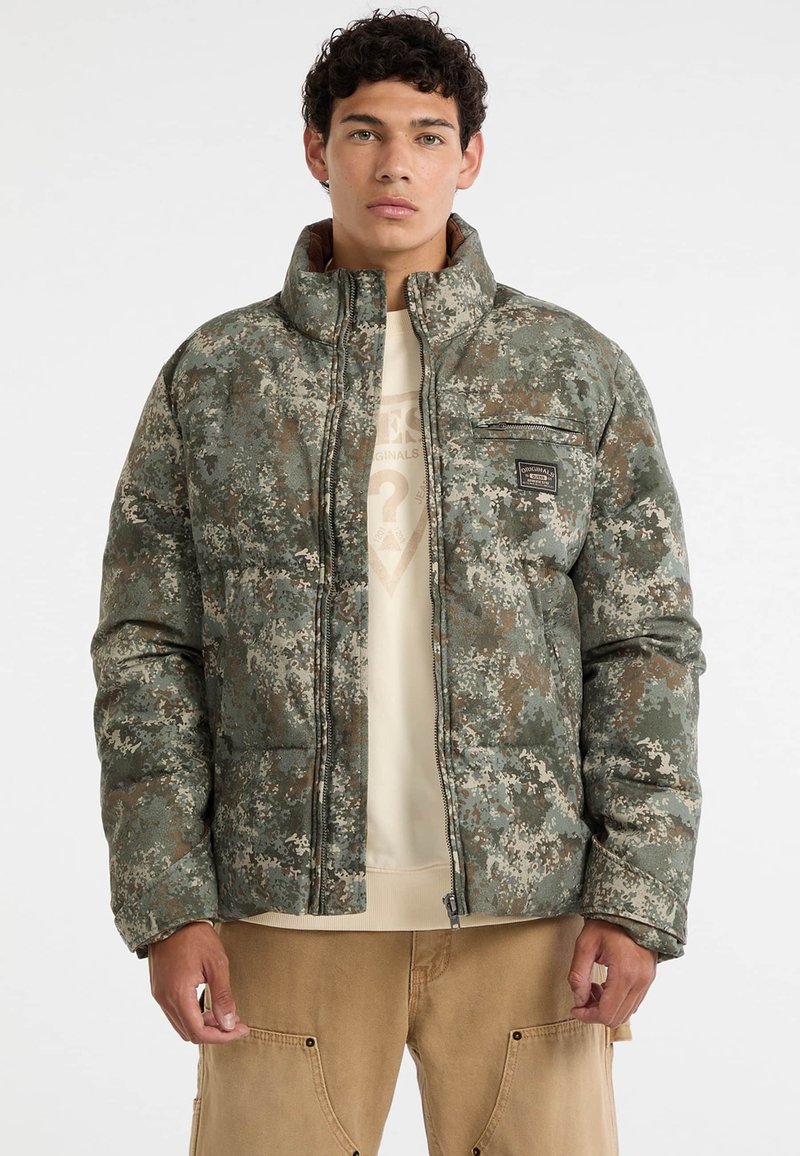 Giacca a vento in design camouflage con colori verde, marrone e crema. Presenta una chiusura a zip, colletto alto e una tasca sul petto.
