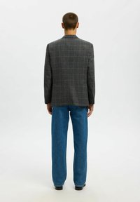 Pelēks pledēts žakete ar piegriezumu, kas aprīkots ar vienu šķēlumu un uzgriežņveida atlokiem, kopā ar vaļīgām zilām džinsa biksēm.