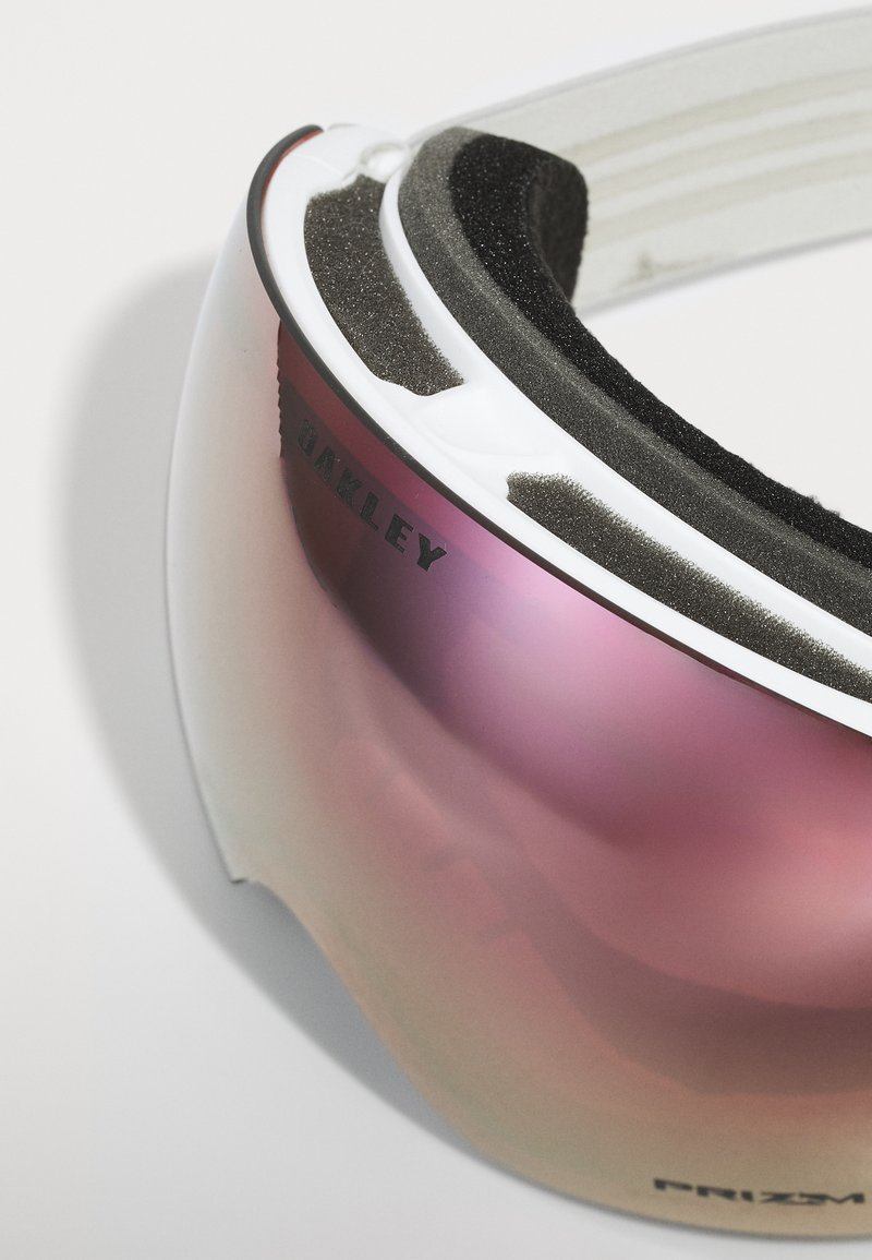Skibrille mit einem weißen Rahmen, pinkem, reflektierendem Glas und weicher schwarzer Schaumstoffpolsterung im Innenbereich für den Komfort. Mit Oakley-Branding.