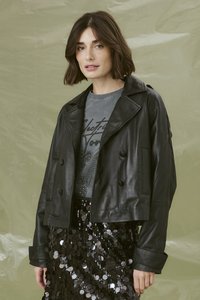 Melnas ādas īsās jakas ar dubultās aizdares dizainu, plašiem atlokiem un sānu kabatām, virs pelēka grafiska t-kreklu un pērļu svārkiem.