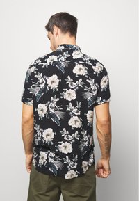 Chemise noire à manches courtes avec un motif floral en rose clair et vert. Présente une coupe décontractée et un col standard.