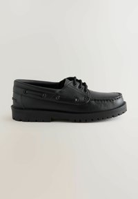 Chaussure bateau en cuir noir avec un bout rond, un système de laçage et une semelle texturée. Présente des coutures visibles et des œillets en métal pour les lacets.