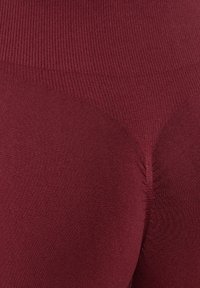 Leggings côtelés bordeaux avec un design sans couture, en tissu doux et extensible, et d'une texture lisse. Pas de motifs ou de matériel visible.