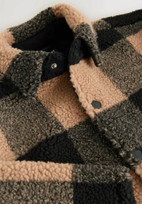 Chaqueta de forro polar en patrón de cuadros en tonos marrón, negro y beige. Cuenta con una tela texturizada, botones a presión y un cuello vuelto.