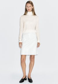 Crèmekleurige trui met lange mouwen en hoge hals, gecombineerd met een wit leren rok tot op de knie en zwarte slingback schoenen. Soepele texturen, minimalistisch ontwerp.