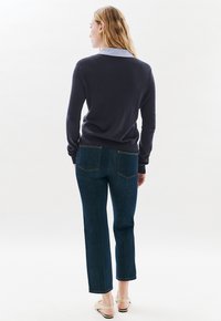 Un pull marin avec un col bleu clair, associé à un jean en denim foncé avec des coutures claires. Des sandales à bride épaisse complètent la tenue.