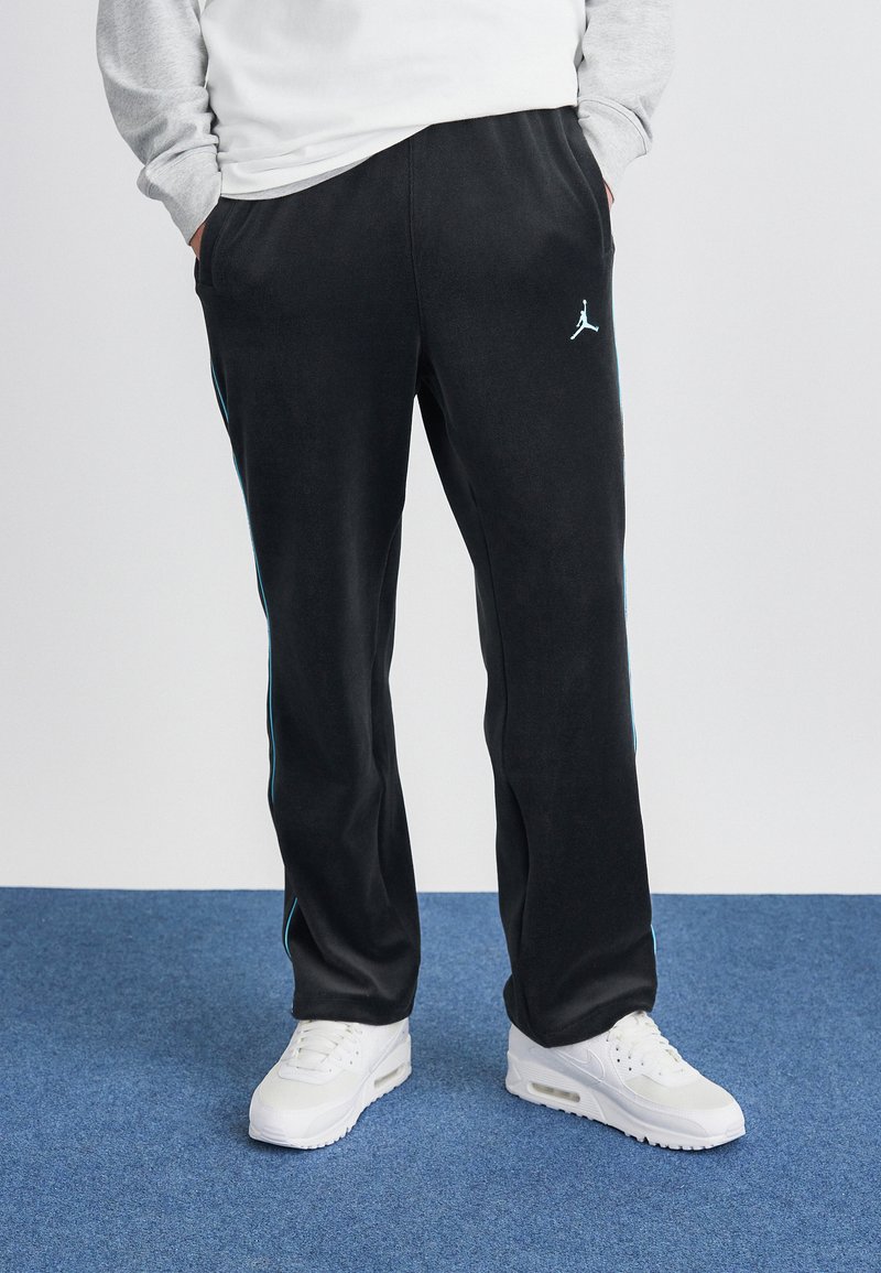 Juodos sportinės kelnės su šoninėmis turkio spalvos juostelėmis ir mažu baltu Jumpman logotipu. Pagamintos iš minkštos, tekstūruotos medžiagos, derinamos su baltomis sportinėmis bateliais.