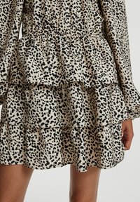 Gestuftes, knielanges Kleid aus beigem Stoff mit schwarzem Leopardenmuster. Es hat lange Ärmel und einen elastischen Taillenzug für einen gerafften Effekt.
