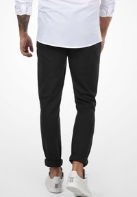 Crne uske hlače od mekog materijala, s prevrnutim rubovima i slim fit krojem, uparene s bijelim tenisicama.