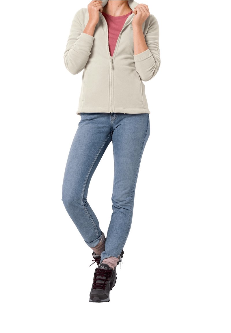 Fleecejacka i ljusgrått med dragkedja fram, bärs över en rosa top, ihop med blå jeans och grå vandringsskor. Mjuk textur och avslappnad stil.