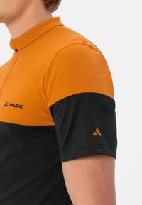 Polo à manches courtes avec une partie supérieure orange et une partie inférieure noire, fabriqué à partir d'un tissu texturé, avec un logo brodé sur la poitrine et la manche.