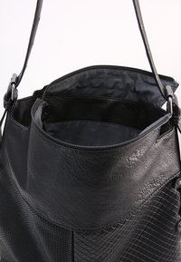 Zwarte schoudertas van gestructureerd leer met een gladde binnenvoering. Beschikt over een ritssluiting en een verstelbare schouderband. Rond ontwerp aan de bovenkant.