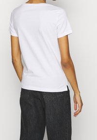 Hvid kortærmet t-shirt med rund hals, glat tekstur, sideslidser ved kanten, parret med mørke højtaljede jeans.