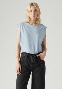 Top senza maniche di un blu chiaro, realizzato in un morbido tessuto testurizzato; abbinato a jeans in denim neri a vita alta con coulisse e tasche.