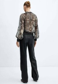 Blusa trasparente a stampa con maniche lunghe e vestibilità ampia, abbinata a pantaloni in pelle neri a vita alta. Dettaglio della schiena aperta visibile.