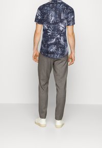 Chemise à manches courtes à boutons avec une base bleu marine et un motif de feuilles blanches ; associée à un pantalon gris et des baskets blanches.