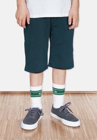 Mörkblå shorts med avslappnad passform, kombinerat med vita strumpor med gröna ränder och grå sneakers med texturerad yta och vita sull.