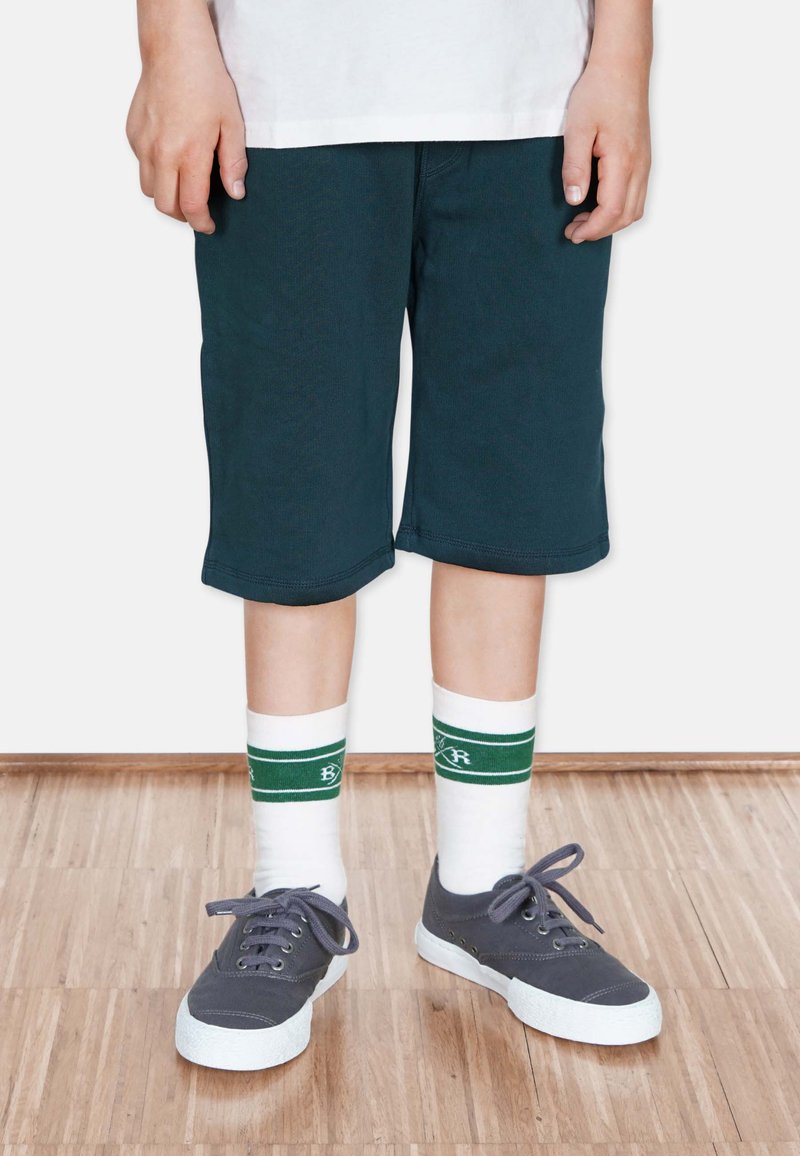 Mörkblå shorts med avslappnad passform, kombinerat med vita strumpor med gröna ränder och grå sneakers med texturerad yta och vita sull.