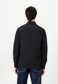 Svart langermet skjorte laget av et glatt materiale, med krage og knappemanchetter, sammen med mørke denimjeans.