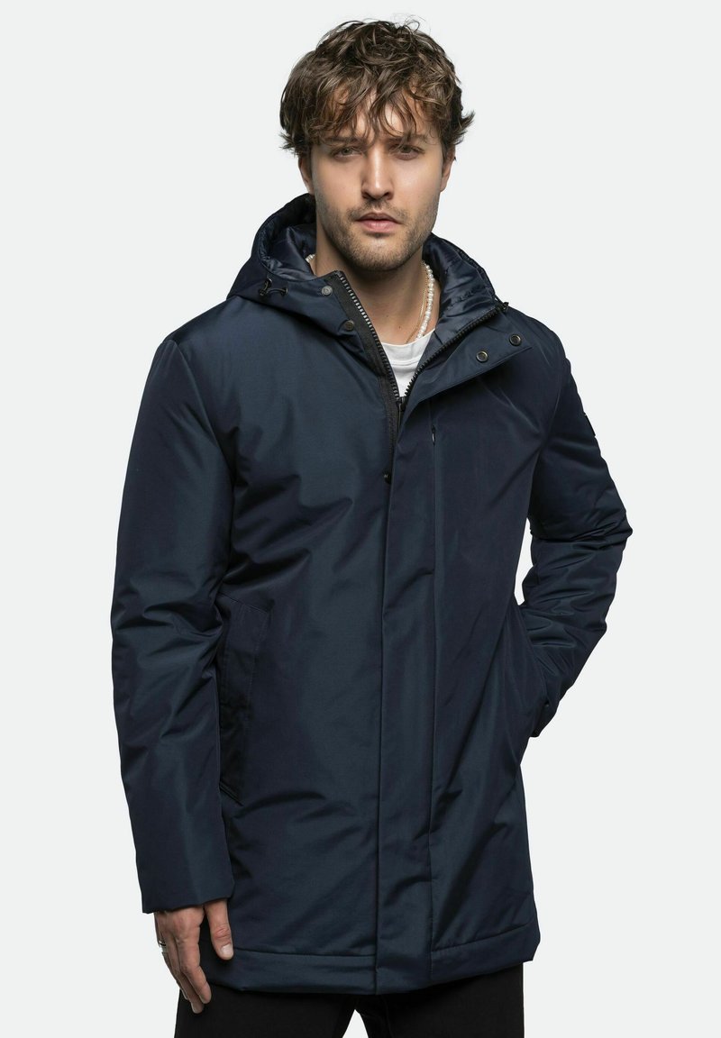 Marineblå parka-jakke med lynlås og knaplukning, forreste lommer, justerbar hætte, glat tekstur og mellemlang design.