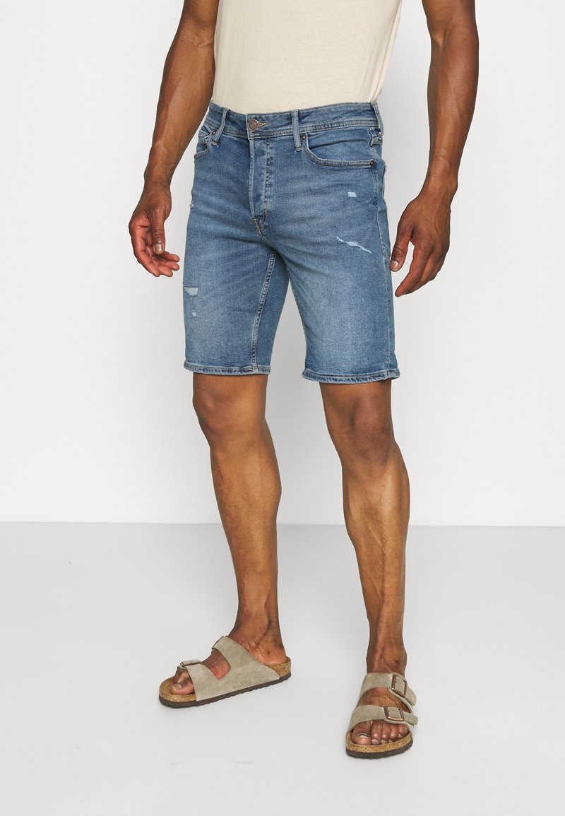 Shorts de mezclilla en azul claro con un diseño desgastado, que cuentan con bolsillos y un corte recto, combinados con sandalias beige.