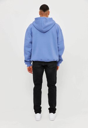 Light blue hooded sweatshirt with a relaxed fit, paired with black jeans and white sneakers. Features a kangaroo pocket and ribbed cuffs.