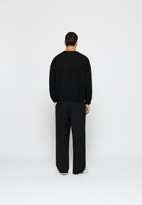 Sweater oversized preto em material texturizado e felpudo, combinado com calças largas pretas. O conjunto apresenta um design minimalista e cores neutras.