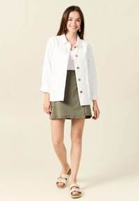 Witte button-up jas, olijfgroene rok en beige sandalen met gespen. Gladde stof, relaxte pasvorm en een eenvoudig ontwerp.