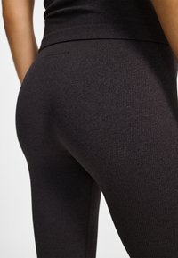 Czarne prążkowane legginsy z wysokim stanem. Materiał jest gładki i przylegający, podkreślający kształt nóg i pośladków.