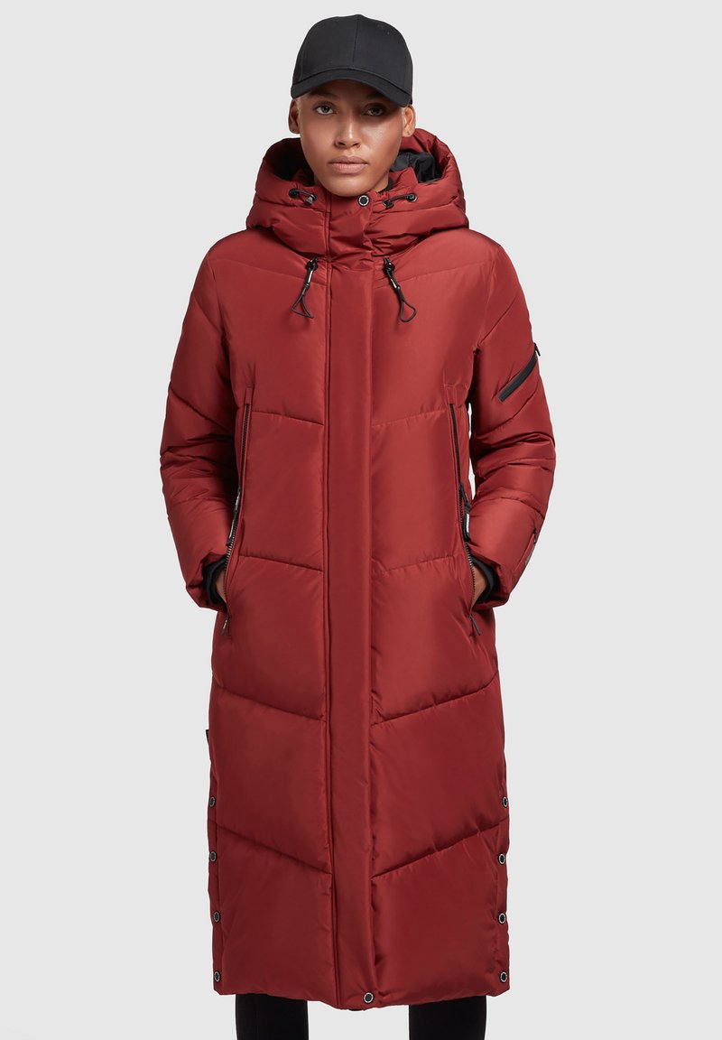 Abrigo acolchado rojo con capucha, bolsillos con cremallera, una silueta larga y detalles de botones a presión en los laterales. Textura suave y material resistente al agua.