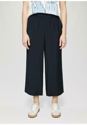 Marineblauwe wijde broek gemaakt van lichte stof, met een elastische tailleband. Gecombineerd met witte sneakers, wat zorgt voor een casual look.