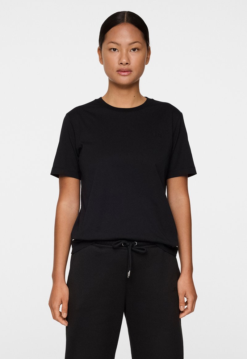 Musta lyhythihainen t-paita pehmeästä puuvillakankaasta, jossa on pyöreä kaula-aukko ja huomaamaton logo rinnassa. Yhdistetty mustiin collegehousuihin.