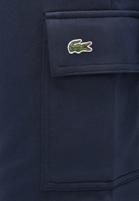 Námornícka mikina s textúrovanou látkou, zabezpečeným vreckom a zeleným vyšívaným logom krokodíla na hornej prednej strane.