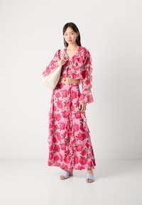 Set composto da crop top floreale e gonna maxi in rosa con stampe di rose rosse. Maniche e orlo a balze. Complementato da sandali azzurri chiari e borsa beige.