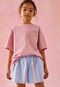 Roze katoenen T-shirt met korte mouwen en een kleine graphic. Lichtblauwe shorts met verticale strepen in roze en wit, textiel met textuur.