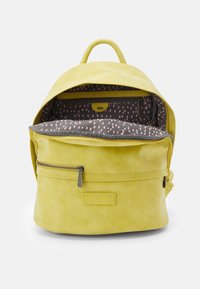 Żółty skórzany plecak z przednią kieszenią na zamek. Otwarta góra ukazuje szare wyściółka w wzory z różowymi akcentami oraz wewnętrzną kieszeń na zamek.