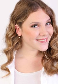 Gouden hoepel oorbellen hebben kleine hangende parels, wat zorgt voor een textuur en gelaagd ontwerp. Het model heeft golvend haar tot op de schouders en draagt een witte blouse.