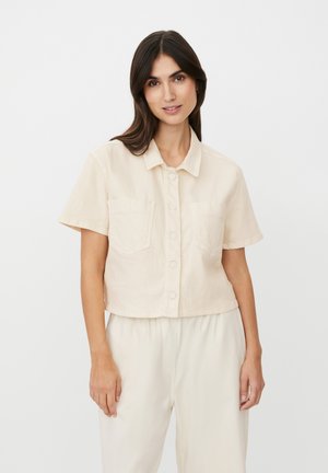Kortærmet skjorte i lysebeige bomuld med croppeffekt, udstyret med spidst krave, knaplukning foran og to brystlommer. Glat tekstur.